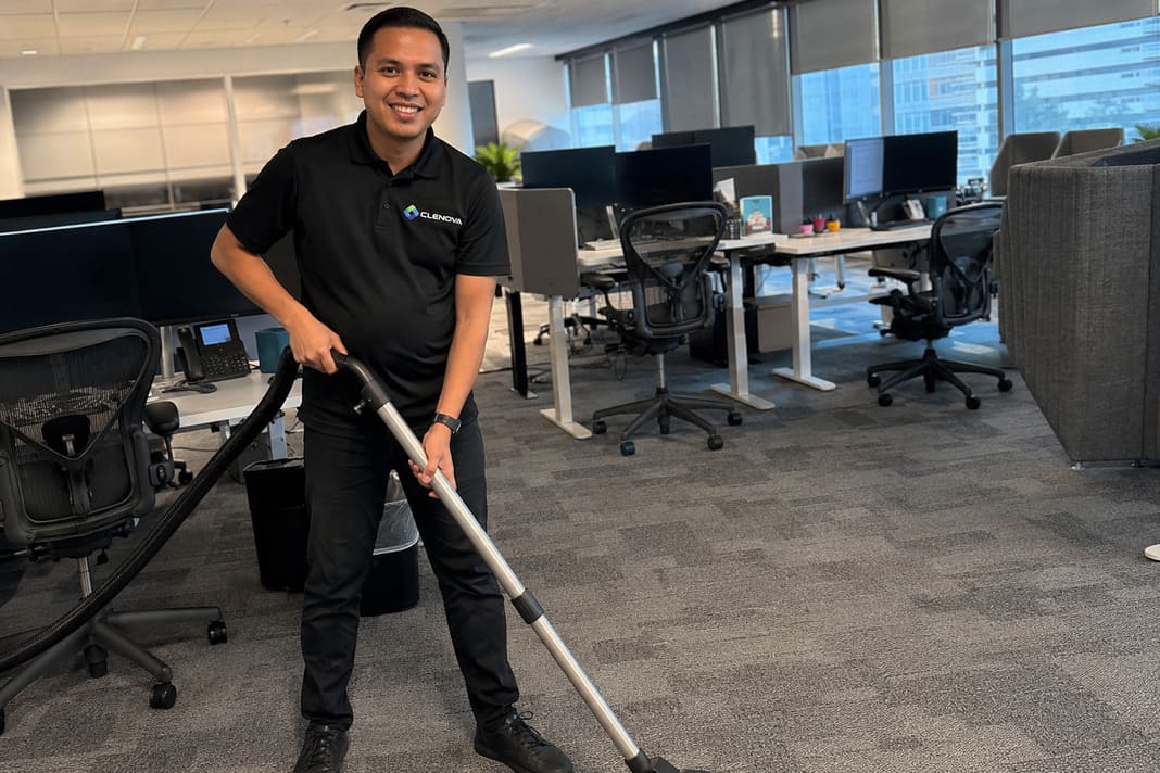 Clenova cleaner in black polo vacuuming carpet floor in a modern office.